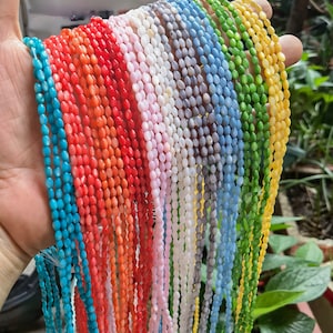 May include: A variety of colors of oval-shaped shell beads strung on thin cords. The beads are in shades of turquoise, blue, green, yellow, orange, red, pink, white, and gray.