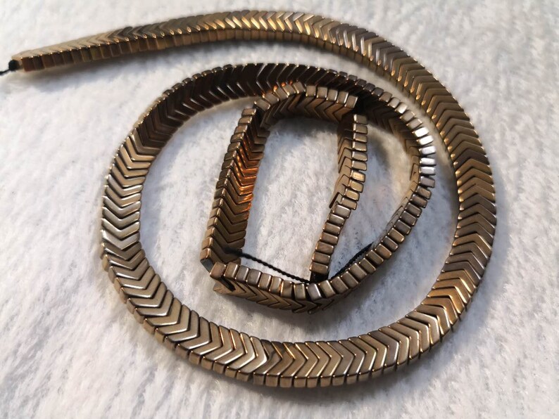 May include: A gold-toned chevron-shaped beaded necklace. The beads are arranged in a zig-zag pattern and are connected by a thin string.