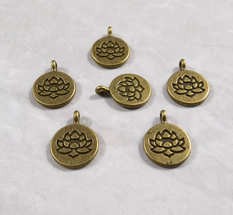 May include: Six antique gold-toned metal charms with a lotus flower design. Each charm has a loop for attaching to a necklace, bracelet, or other jewelry.