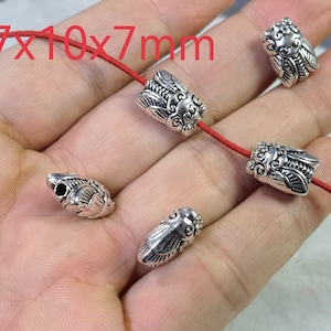 Puede incluir: Cuentas de metal de color plateado con forma de cigarra, que miden 13,7x10x7mm cada una. Las cuentas presentan grabados detallados en las alas y el cuerpo. Dos cuentas están ensartadas en un cordón rojo fino y hay dos cuentas sueltas.