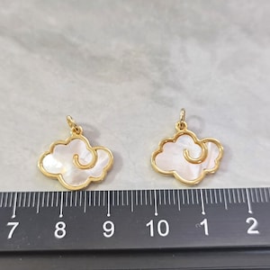 May include: Two gold-tone cloud-shaped charms with white mother-of-pearl inlays. The charms are about 1 inch wide and have a loop at the top for attaching to a necklace or bracelet.