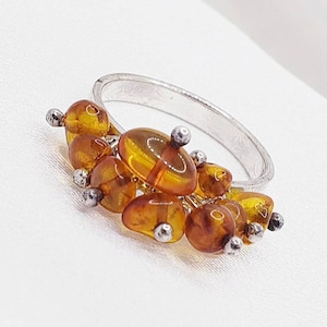 May include: A silver ring with multiple amber stones set in a cluster around the band.