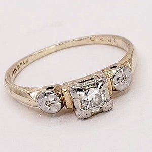 May include: A gold band ring with a single diamond set in a square prong setting. The ring has two smaller diamonds on either side of the center stone.
