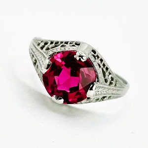 Puede incluir: Un anillo de filigrana de plata con una gran piedra preciosa roja rubí facetada.