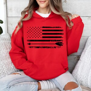May include: Red hooded sweatshirt with a black and white distressed American flag design and an arrow with feathers.