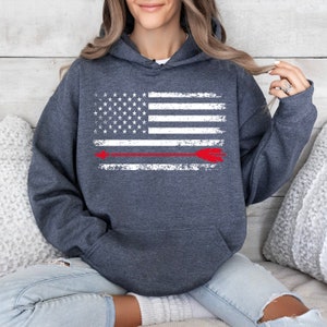 May include: A dark gray hooded sweatshirt with a distressed white American flag design and a red arrow across the center.