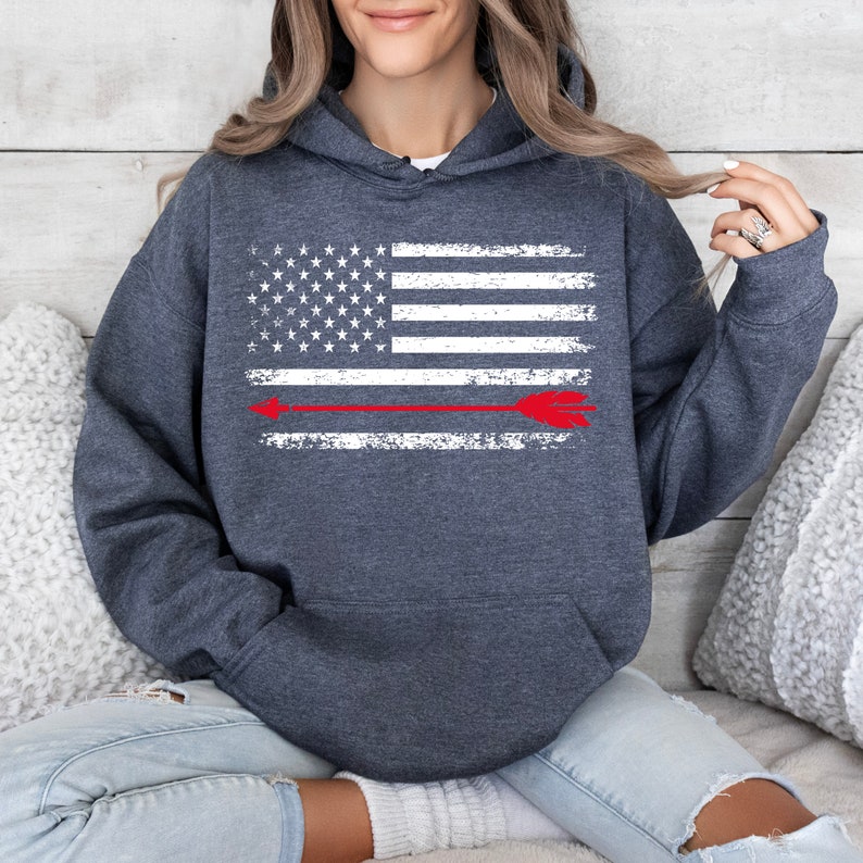 May include: A dark gray hooded sweatshirt with a distressed white American flag design and a red arrow across the center.