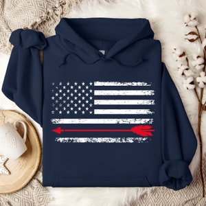 May include: A navy blue hoodie with a distressed white American flag design and a red arrow across the middle.