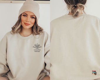 May include: A beige sweatshirt with a black and white graphic of an open book with flowers on top. The text "Custom Book Club Name" is below the graphic.