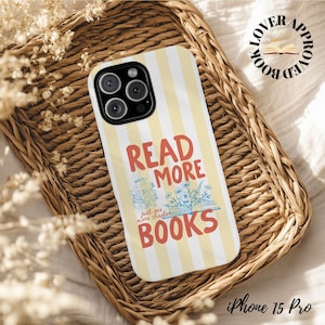 May include: A yellow and white striped iPhone 15 Pro case with the words "READ MORE BOOKS" in red and blue. The case features a stack of books and floral illustrations. The case is on a woven basket.