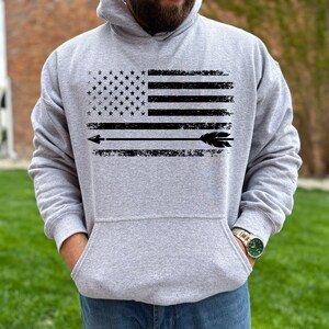 May include: A gray hooded sweatshirt with a distressed black and white American flag design and an arrow pointing to the right.