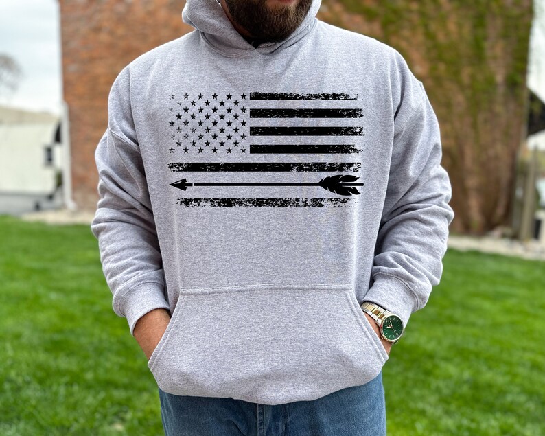 May include: A gray hooded sweatshirt with a distressed black and white American flag design and an arrow pointing to the right.