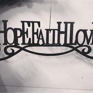 Puede incluir: Decoración de pared de metal negro con las palabras "Hope Faith Love" en una fuente decorativa.