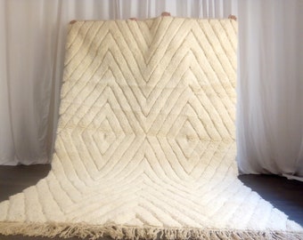 May include: A white, fluffy rug with a diamond pattern. The rug has a fringe border.