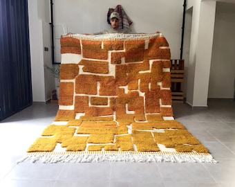 May include: A large, hand-woven rug with a geometric pattern of white and mustard yellow squares. The rug has a fringe border.