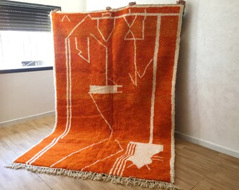 May include: A large, orange and white Moroccan rug with a geometric pattern. The rug has a fringe border and is made of wool.