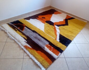 May include: A large, rectangular rug with a geometric pattern in shades of white, orange, brown, and yellow. The rug has a fringe border.