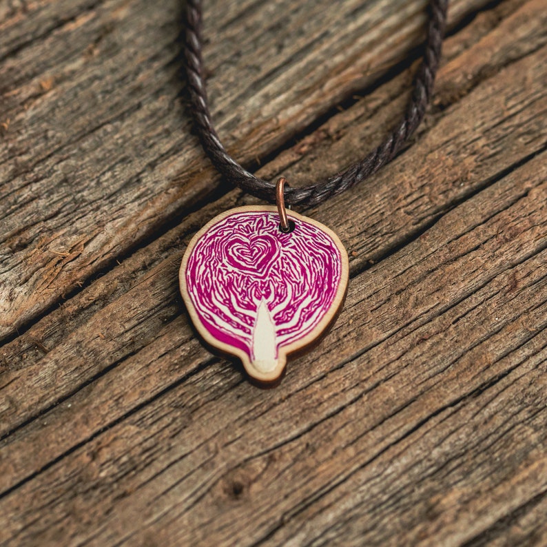 A necklace featuring an original painting of a halved cabbage with a small heart in it, printed on a die-cut wooden pendant. The cord is brown vegan-friendly waxed cotton.