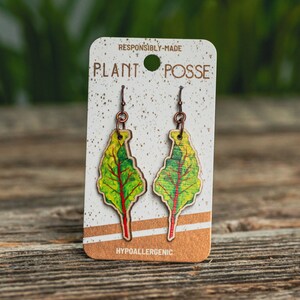 Dangle earrings with an original painting of a chard leaf printed on die-cut wood. The earrings are symmetric to one another.