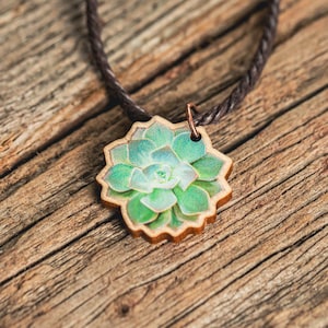 A necklace featuring an original painting of a succulent, as seen from above, printed on a die-cut wooden pendant. The cord is brown vegan-friendly waxed cotton.