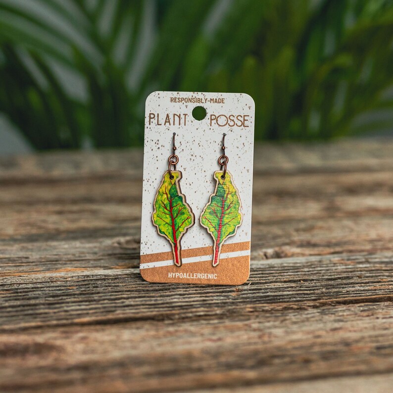 Puede incluir: Un par de pendientes en forma de hoja verde y roja con ganchos de cobre. Los pendientes est&aacute;n en una tarjeta que dice "Plant Posse hecho de forma responsable" e "Hipoalerg&eacute;nico".