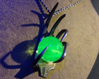 May include: A silver necklace with a hand-shaped pendant holding a bright green glass orb.