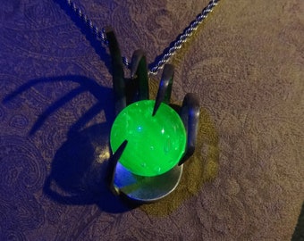 May include: A silver chain necklace with a pendant shaped like a hand holding a green glass orb.