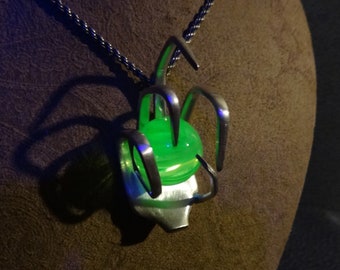 May include: A silver necklace with a pendant made from a twisted metal design that encloses a bright green glass orb.