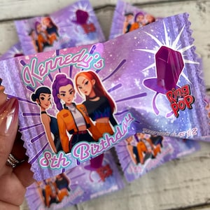 May include: Purple candy wrappers with a Ring Pop design and the text "Kennedy's 8th Birthday". The wrappers feature illustrations of three girls and a large purple ring. Several wrappers are visible.