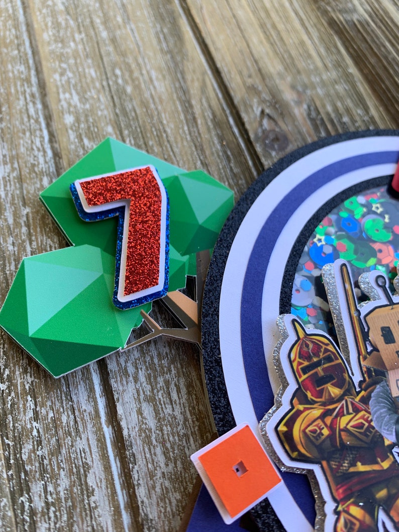 Pu&ograve; includere: Un numero sette rosso con glitter, una forma geometrica verde e un cerchio blu e argento con glitter con un cavaliere e una spada. Il cerchio ha un bordo nero e uno sfondo bianco. C'&egrave; anche un piccolo quadrato arancione con un quadrato nero al centro.