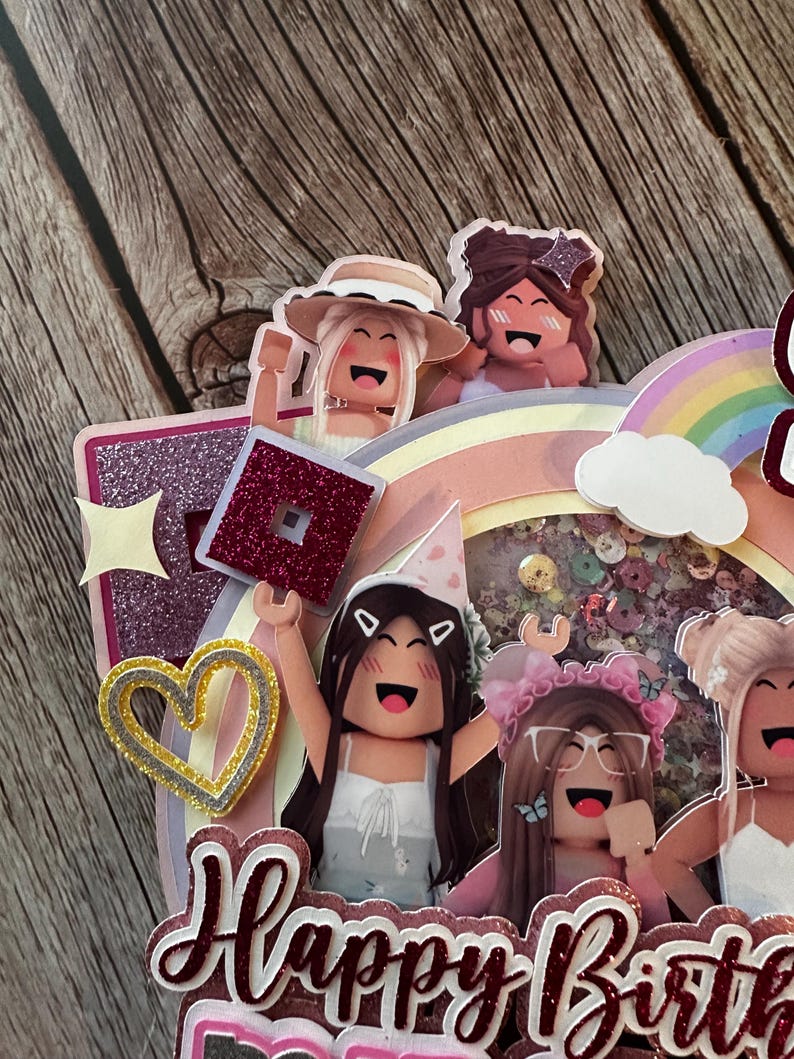 May include: A pink, purple and yellow cake topper with a rainbow, a cloud and four cartoon figures. The figures are holding a red and pink block with a star on top. The cake topper says "Happy Birthday".