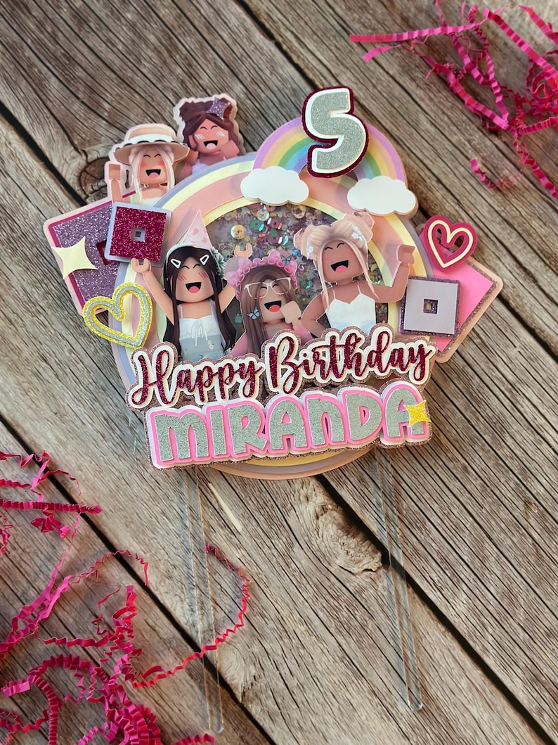 May include: A pink and white cake topper with a rainbow, clouds, and four cartoon figures. The topper says "Happy Birthday Miranda" and has a star and a heart.