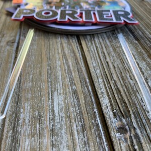 Pu&ograve; includere: Un topper per torta a pi&ugrave; livelli con un personaggio dei cartoni animati con il nome "Porter" in lettere rosse e nere. Il topper &egrave; decorato con una variet&agrave; di colori e disegni.