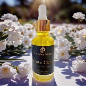May include: A gold and black bottle of Mental Clarity Spiritual Oil Blend by The Healing Priestess. The bottle is 30 ml or 1 fl oz. The bottle is sitting on a white surface with white flowers in the background.