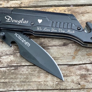 May include: Black multi-tool knife with a partially open blade. The knife has the name "Douglas", a heart symbol, and the phrase "We Love You Very Much" engraved on it. The knife also has a bottle opener and a seat belt cutter.