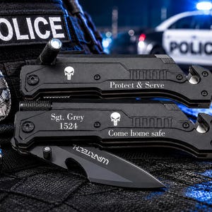 May include: Two black multi-tools with skull emblems and the phrases "Protect & Serve" and "Come home safe". A police badge and a "POLICE" patch are also visible. A police car is in the background.