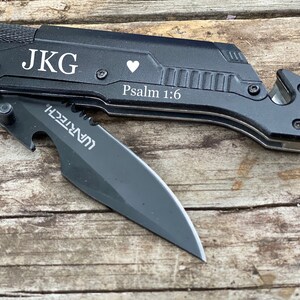 May include: Black multi-tool knife with a partially open blade. The knife has the initials "JKG", a heart symbol, and the text "Psalm 1:6" engraved on the handle. The blade has the "WARTECH" logo.