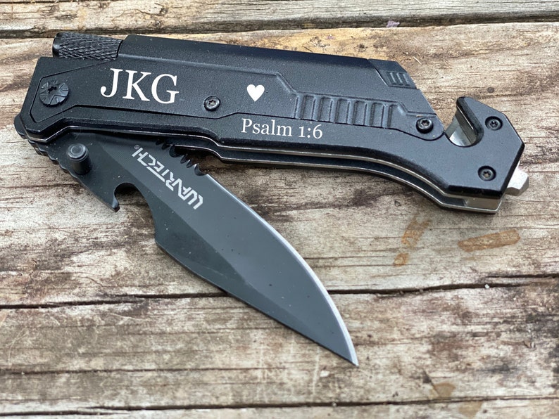 May include: Black multi-tool knife with a partially open blade. The knife has the initials "JKG", a heart symbol, and the text "Psalm 1:6" engraved on the handle. The blade has the "WARTECH" logo.