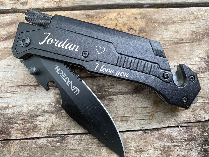 May include: Black multi-tool knife with a partially open blade. The knife has the name "Jordan", a heart symbol, and the phrase "I love you" engraved on it. The blade has the word "WARTECH" printed on it.