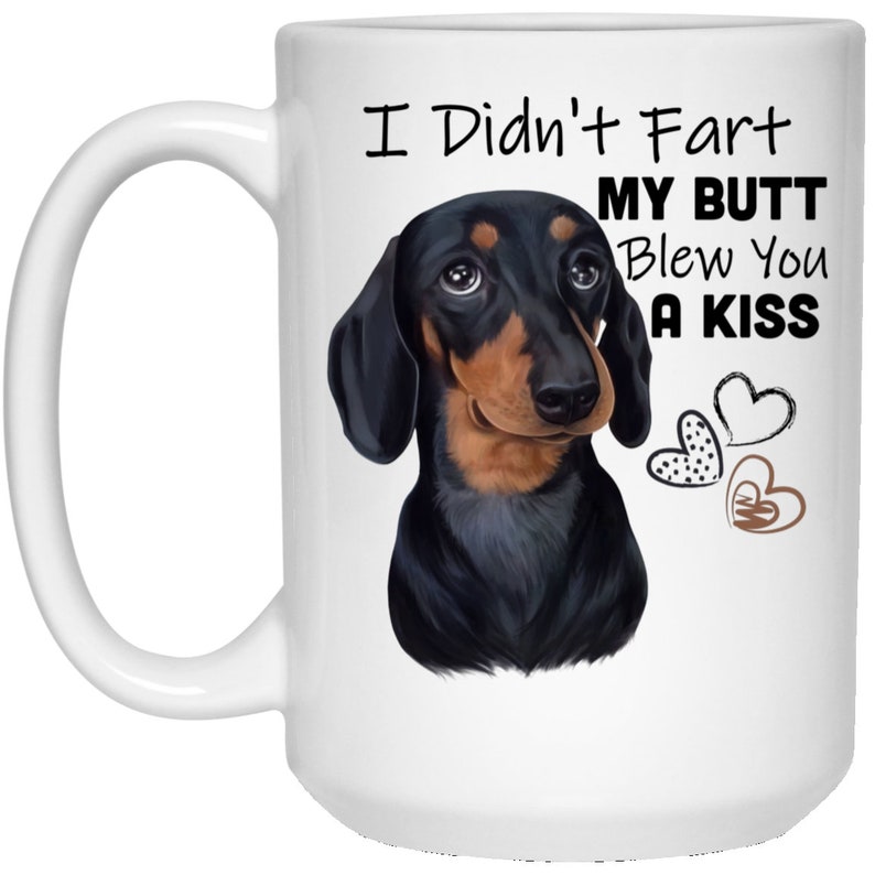 May include: White ceramic coffee mug featuring a black and tan dachshund illustration. The text on the mug reads "I Didn't Fart My Butt Blew You A Kiss" with three brown hearts.