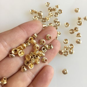 May include: A selection of small, gold-coloured spiral beads. The beads have a conical shape with a central hole and are scattered across a surface. These beads are likely used for jewellery making or other craft projects.