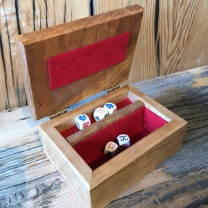 May include: A wooden box with a red felt lining and a hinged lid. The box contains five dice with different coloured dots.