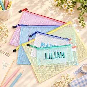 May include: A collection of four rectangular mesh zip pouches in pink, blue, yellow, and white. The smallest white pouch features the name LILIAN printed in bold teal letters. Each pouch has a matching coloured zip with a black pull tab.