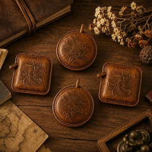 Peut inclure: Quatre rubans à mesurer en cuir marron avec des motifs floraux en relief. Deux rubans sont circulaires et deux sont carrés, chacun doté d'une petite languette sur le côté. Le cuir présente une finition brun clair riche avec des motifs de feuilles.