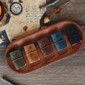 May include: Five small leather-bound journals arranged in a wooden tray. Each journal features a unique floral line art illustration on the cover and is secured with a thin elastic band. The colours include olive green, tan, brown, blue, and black.