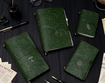 May include: A collection of green leather journals with embossed floral patterns. Each journal is secured with a leather strap and a decorative charm. The journals vary in size and are arranged on a dark surface with pens, glasses, and other stationery items.