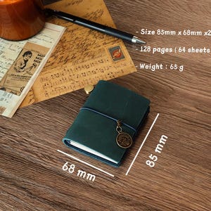 Może przedstawiać: Zielony notes sk&oacute;rzany z niebieskim sznurkiem i metalowym brelokiem. Notes ma wymiary 8,5 cm x 6,8 cm i grubość 2 cm. Zawiera 128 stron (64 arkuszy) i waży 65 gram&oacute;w.