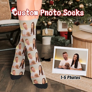 May include: Custom Photo Socks are displayed, featuring a repeating pattern of a couple and a dog. The socks are beige with black heels and toes. The image also includes a polaroid-style photo with the text "1-5 Photos" and the words "Custom Photo Socks" in red.