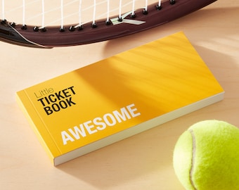 May include: A yellow booklet with the text "Little Ticket Book" and "AWESOME" printed on the front. A tennis ball is in the foreground.