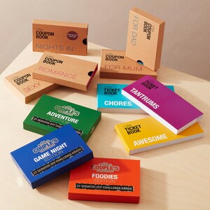 May include: A collection of colorful boxes with different titles, including "Couples Challenge" and "Little Ticket Book". The boxes feature various themes, such as "Adventure", "Game Night", "Foodies", "Tantrums", "Chores", and "Awesome".